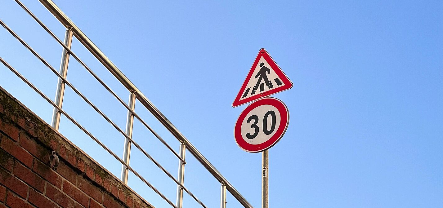 Das Bild zeigt ein Verkehrsschild für eine "Tempo 30"-Zone und sowie ein Schild für einen Fußgängerüberweg