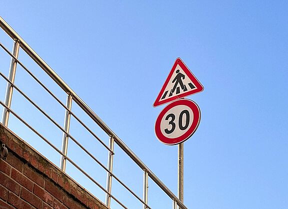 Das Bild zeigt ein Verkehrsschild für eine "Tempo 30"-Zone und sowie ein Schild für einen Fußgängerüberweg