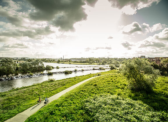 Panoramablick aus der Vogelperspektive auf den Ruhrtalradweg entlang der Ruhr, zwei Radfahrende fahren der Nachmittagssonne entgegen.